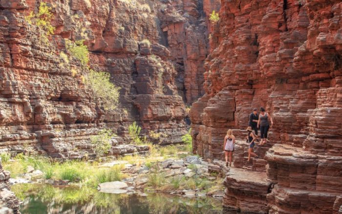 Deep gorge with red rocky walls and people walking along the trail in the distance